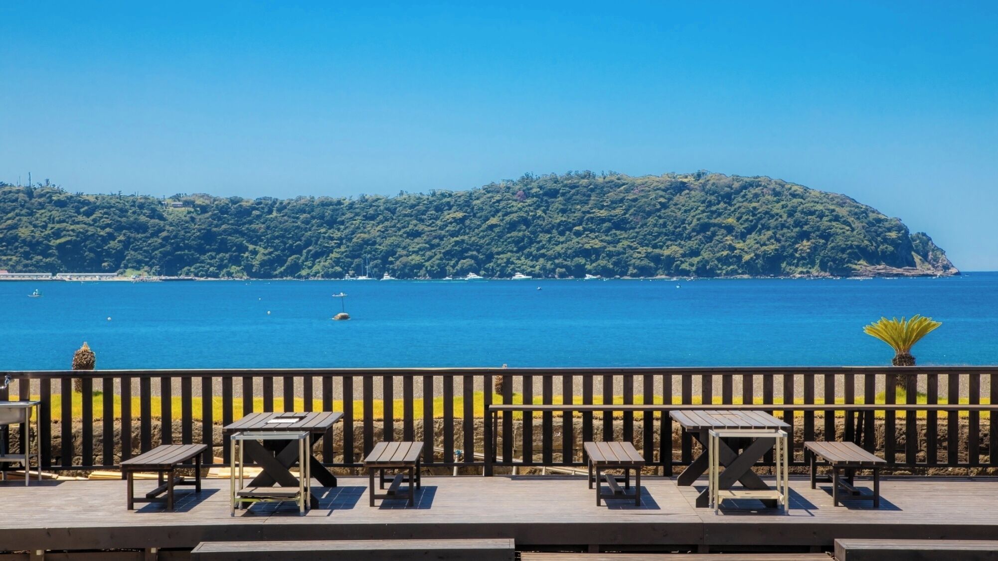 A wooden deck with tables and chairs overlooking a clear blue sea and a forested island.