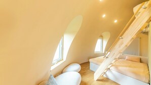 Une chambre de style loft moderne, avec un plafond en pente, un escalier en bois intégré et une grande fenêtre laissant entrer la lumière naturelle.