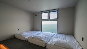 A small, modern room with two single beds aligned against a wall, a large window providing a view of the sea, and a simple, uncluttered design. - Cliff Villa (Konan)