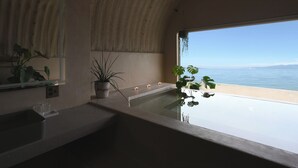 A modern bathroom with a large bathtub, a sink, and a mirror. There are potted plants and candles on the counter. - Covo Ushimado (Setouchi)