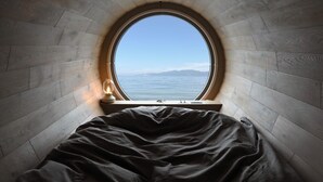 A circular window in a room with a bed and a nightstand. - Covo Ushimado (Setouchi)