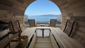 A wooden interior with a circular view of the sea, two wooden chairs, a table, and a wooden bench. - Covo Ushimado (Setouchi)