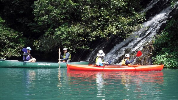 Three kayakers in a river with a waterfall in the background.