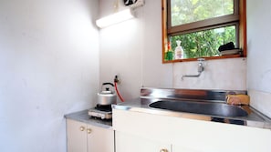 A small kitchen with a stainless steel sink, a kettle, and a window with a view of greenery.