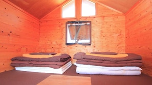 A cozy cabin room with wooden walls, a small window, and two beds with folded blankets.