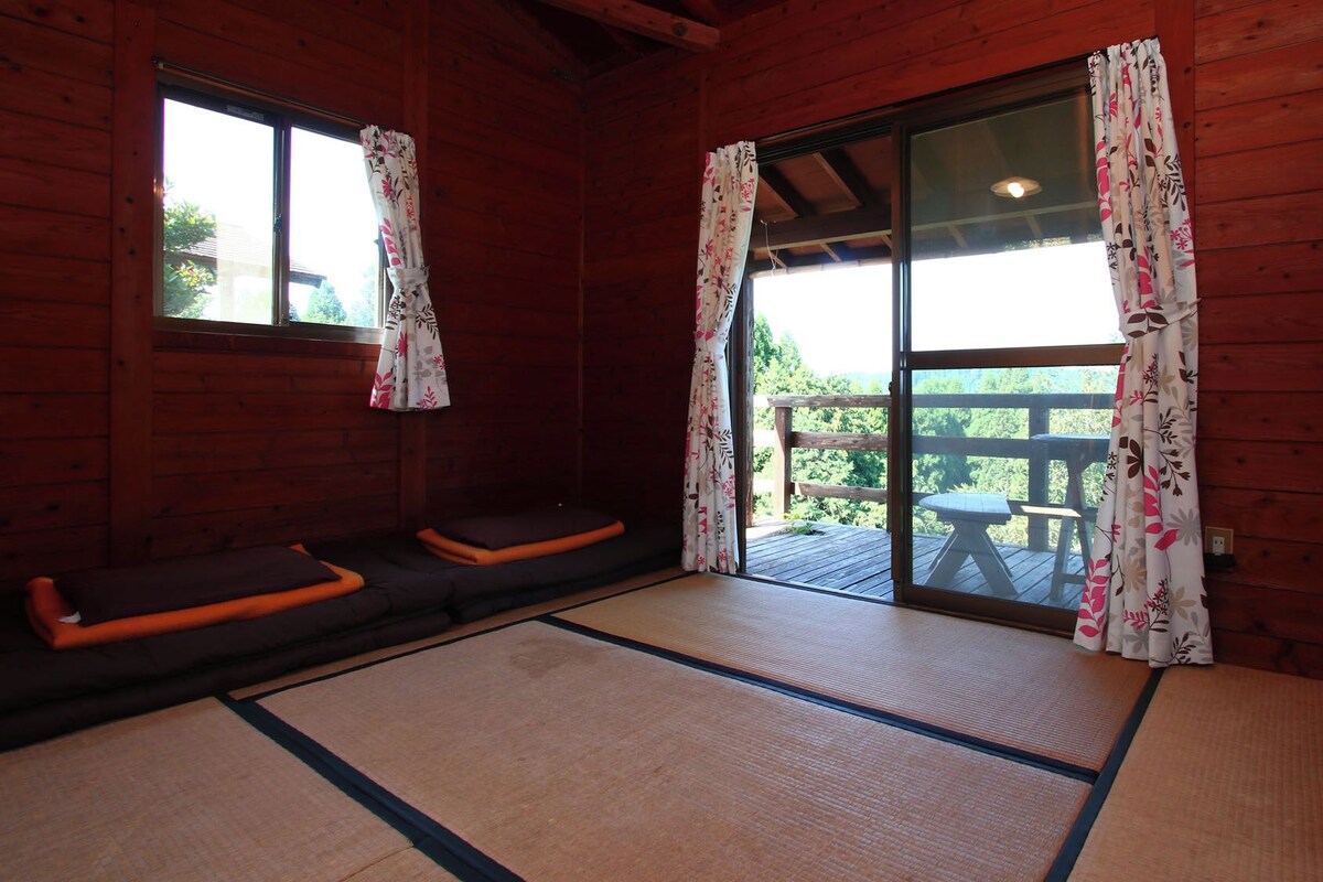A room with tatami mats, a sliding glass door, and a view of a wooden deck and greenery outside.