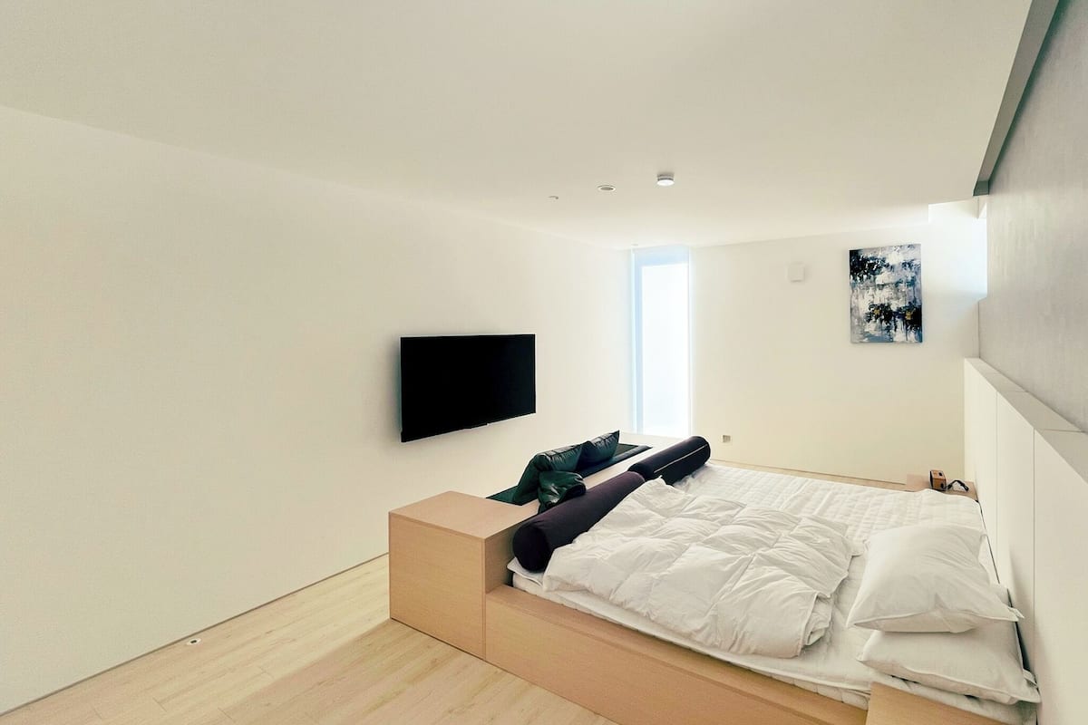 Un dormitorio moderno con cama, televisor y ventana.