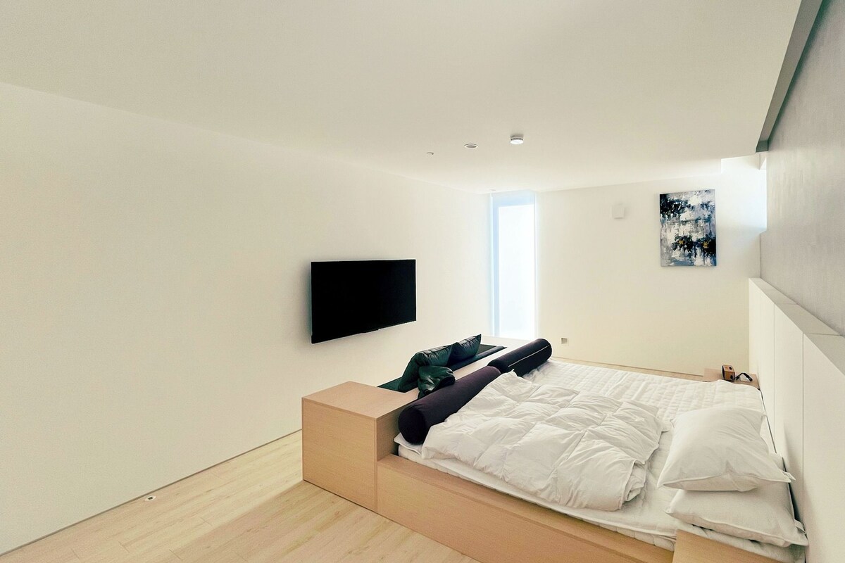 Un dormitorio moderno con cama, televisor y ventana.