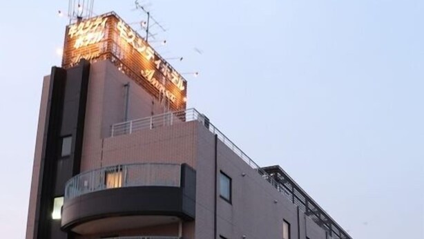 A multi-story hotel with balconies, a sign indicating a restaurant, and a parking area with cars. - Ushiku City Hotel Honkan Annex (Ushiku)