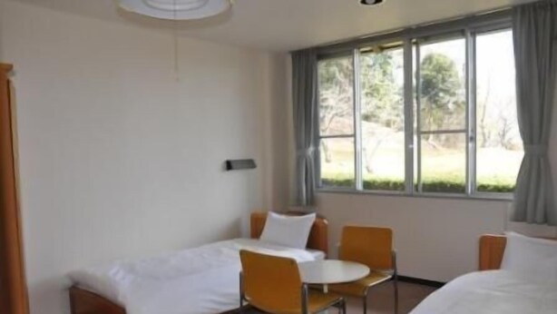 Quarto de hotel com cama, uma mesinha, duas cadeiras e uma janela com cortinas.