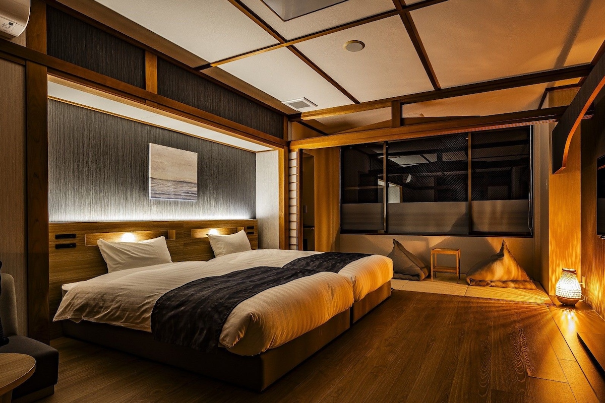 A modern hotel room with a large bed, a bedside table, a chair, and a window with a view.