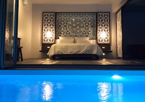 A bedroom with a pool view, featuring a bed, decorative wall panels, and two wall-mounted lights.