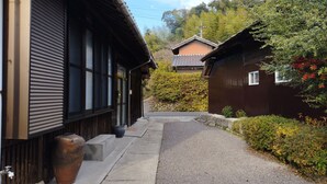 A narrow pathway leading to traditional wooden buildings with large windows and a stone pathway. - Kominka Hashinoya (Yusui)