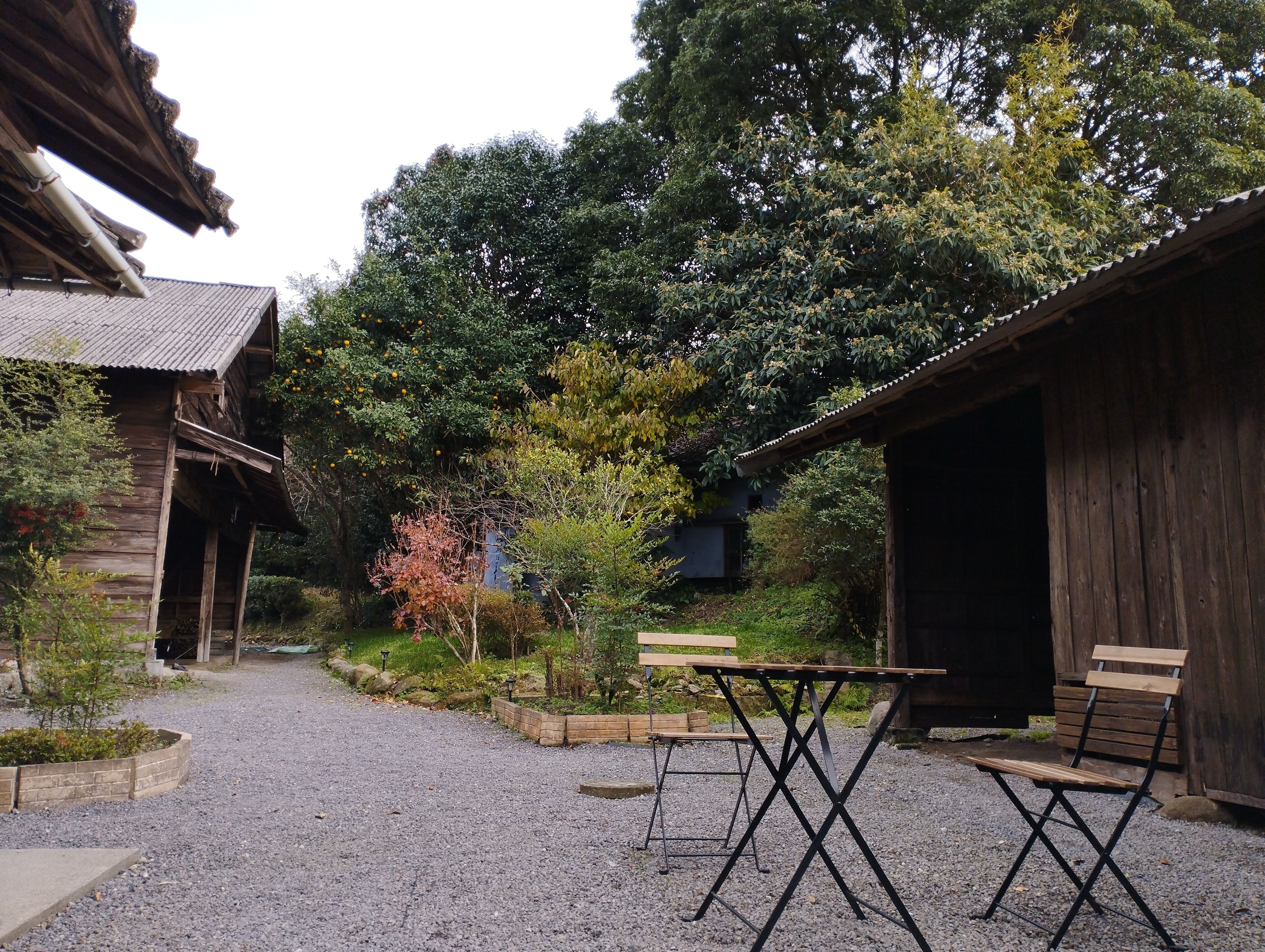 A rustic wooden building with a gravel courtyard, a wooden table, and two chairs.