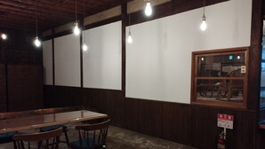 A restaurant interior with a wooden table, chairs, hanging light bulbs, a fire extinguisher, and a window with a view. - Kominka Hashinoya (Yusui)