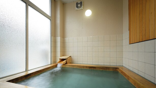 Ein Thermalbad mit einer Holzbank, gefliesten Wänden und einem Fenster.