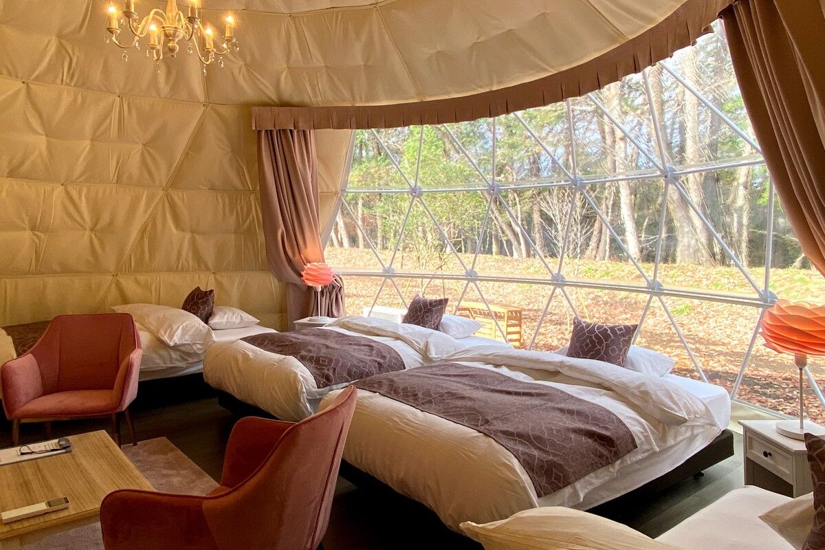 Une chambre confortable avec deux lits, un lustre et une grande fenêtre donnant sur la forêt.