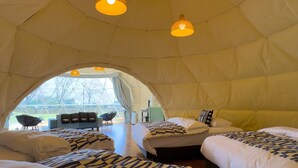 Ein geräumiges Zelt-ähnliches Zimmer mit drei Betten, einem Schlafsofa und einem Essbereich.
