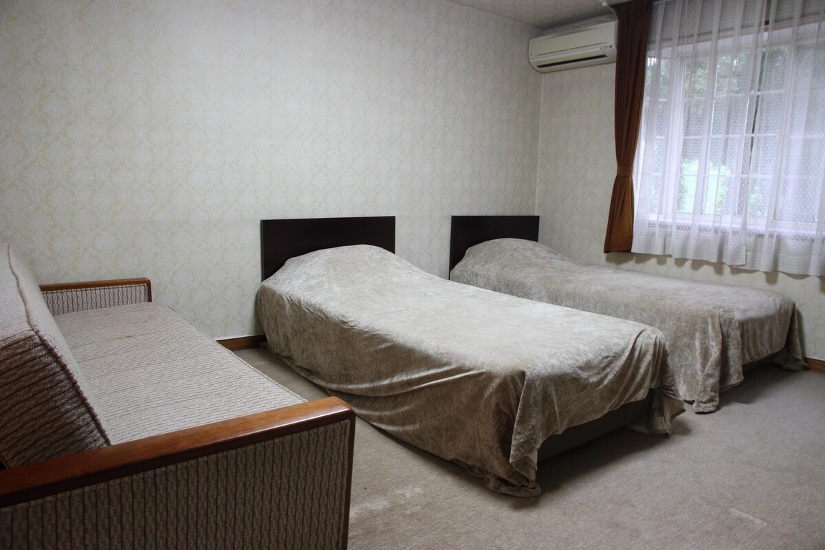 A room with two single beds, a sofa, and a window with curtains.