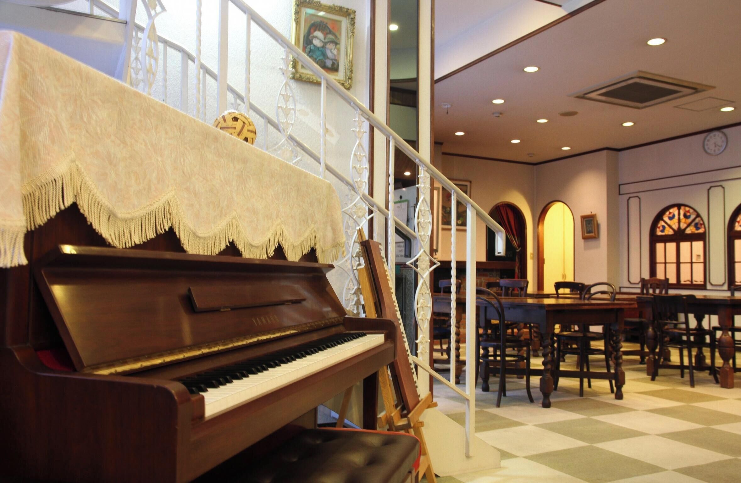 Un piano en una habitación con suelo a cuadros, sillas de madera y una escalera.