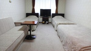 Una habitación pequeña y luminosa con sofá, dos camas individuales, una mesa y televisor.