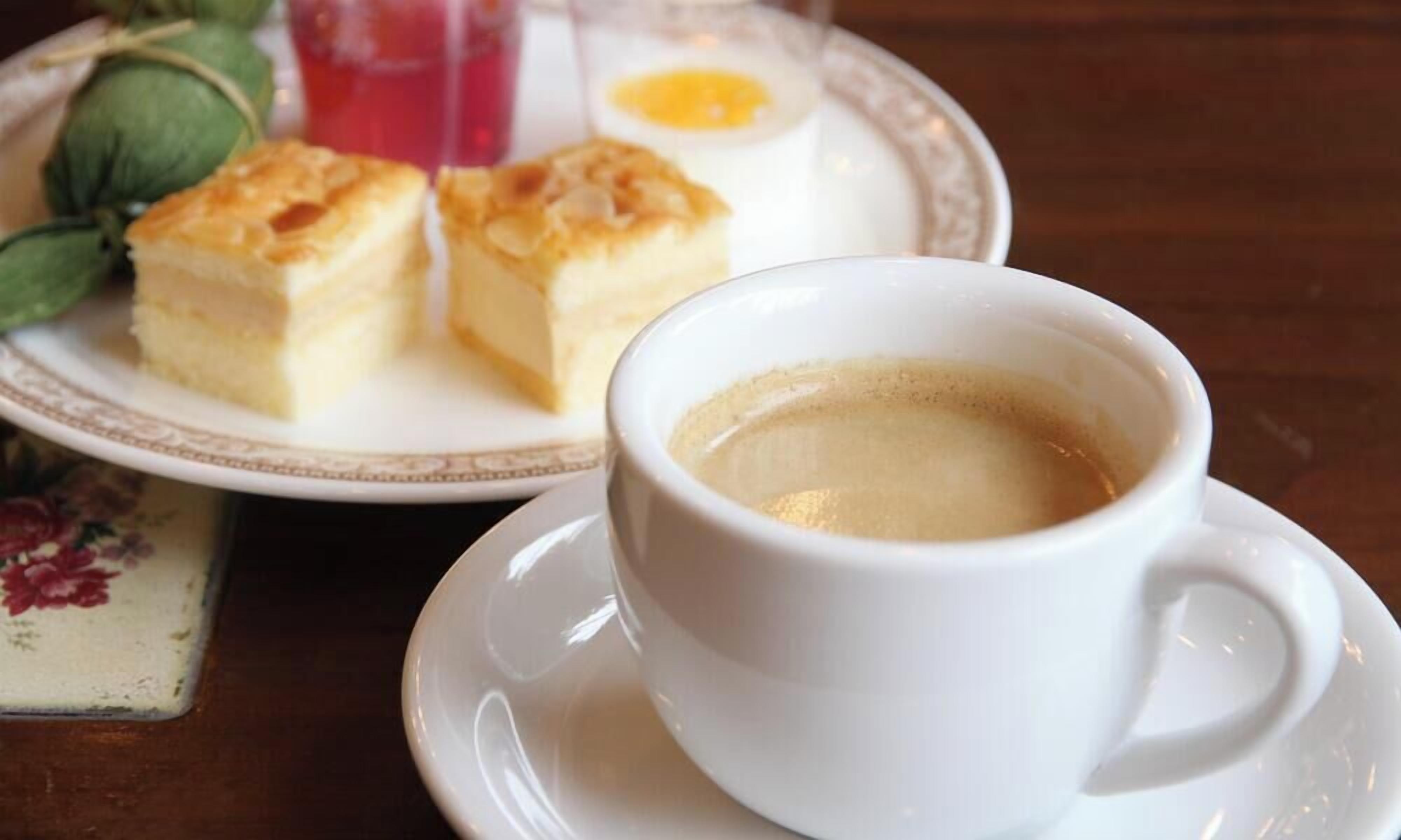 A cup of coffee and a plate with pastries and a boiled egg on a table.