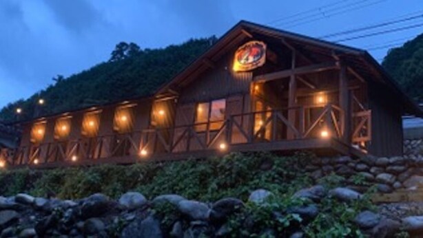 Un edificio de madera con un letrero grande iluminado, rodeado de rocas y vegetación.