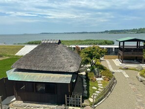 Un bâtiment de style japonais traditionnel, doté d’un toit de chaume, d’une terrasse en bois et offrant une vue sur la mer.