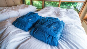 Ein Bett mit weißen Leinen und zwei blauen Handtüchern, versehen mit einem kleinen Emblem, vor einem Fenster mit Blick auf Grünflächen.