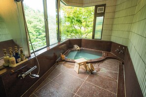 A spa room with a hot tub, a wooden stool, and a window with a view of trees. - Villa Tombo Hakone (Hakone)