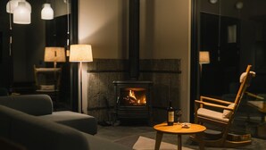 Une pièce chaleureuse avec une cheminée, un canapé, un fauteuil et une table sur laquelle se trouvent une bouteille et un verre.