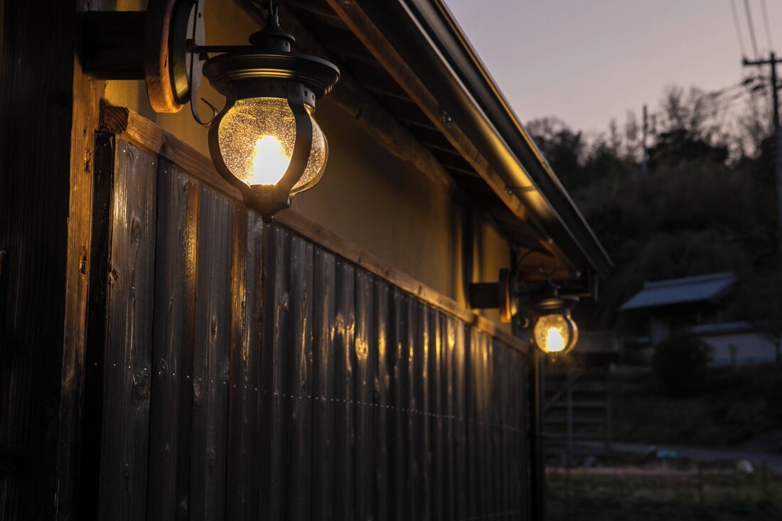 A wooden building with a corrugated metal exterior and a single lit lantern hanging from the roof.