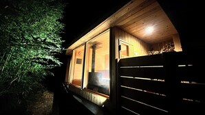 A wooden cabin with a large window, a door, and a stack of firewood inside. - Akiya Cornerstone (Awaji)