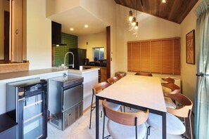 A modern kitchen with a central island, built-in appliances, and a dining area with a long table and chairs. - Maigre Hoodstar (Ito)