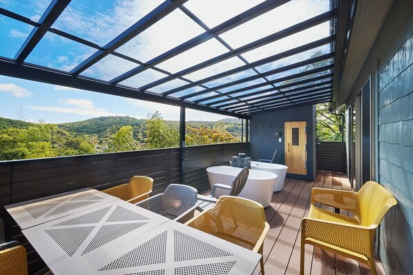 An outdoor patio with a glass ceiling, wooden deck, and seating area with tables and chairs. - Maigre Hoodstar (Ito)