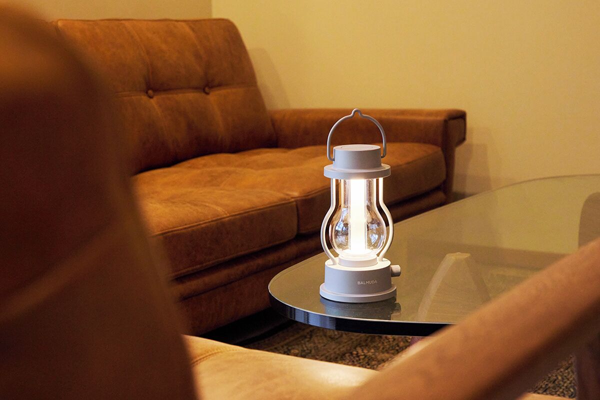Un salon moderne avec une table basse en verre, un canapé en cuir marron et une lampe de style lanterne, de couleur blanche.