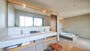 Uma casa de banho moderna com duas pias, um espelho grande, uma banheira e um banquinho de madeira.