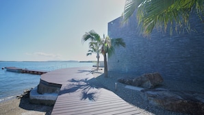 A wooden deck leading to a beach with a palm tree and a stone wall. - Lentement Suite-villa Awaji (Sumoto)