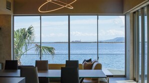 Uma sala de jantar moderna com uma janela ampla que oferece vista para um mar tranquilo e montanhas ao longe.