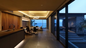 A modern kitchen with a central island, dining area with chairs, and large sliding glass doors leading to a balcony with a view of the ocean. - Lentement Suite-villa Awaji (Sumoto)