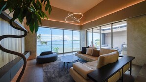 A modern living room with a large window overlooking a body of water, a sofa, a coffee table, and a hanging light fixture. - Lentement Suite-villa Awaji (Sumoto)