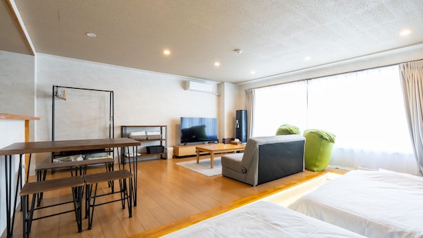 Een moderne hotelkamer met houten vloer, een flatscreen televisie, een bank, een eettafel met banken en een groot raam met gordijnen.