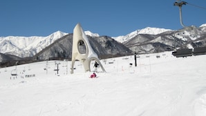 Une piste de ski enneigée, dotée d’une structure architecturale unique, de remontées mécaniques et surplombée d’un ciel bleu azur.