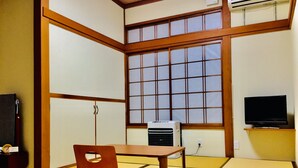 A traditional Japanese room with tatami flooring, a low table with a cushion, a television on a stand, and a sliding door. - Marufuku Ryokan (Yokote)