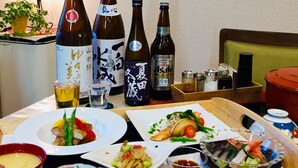 A dining table with various dishes, including sushi and a bowl of soup, and several bottles of sake. - Marufuku Ryokan (Yokote)