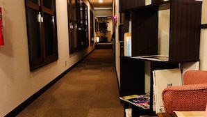 A hotel corridor with a carpeted floor, wooden doors, and a seating area with a table and chairs. - Marufuku Ryokan (Yokote)