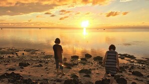 Two individuals standing on a rocky beach with a sunset in the background. - Minshuku Irayoi (Ishigaki)