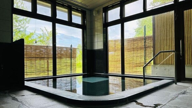 Ein moderner, überdachter Pool mit großen Fenstern, Steinboden und einem Bambuszaun im Außenbereich.