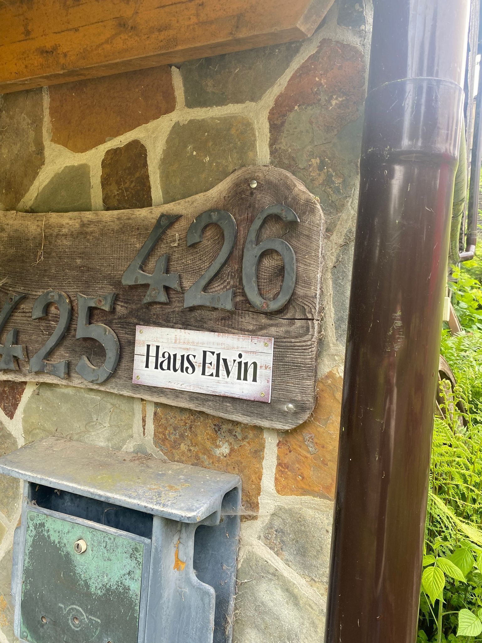 Ein Hausnummernschild mit der Aufschrift '426' und 'Haus Elvin' an einer Steinmauer.