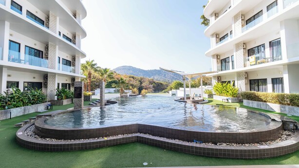 A hotel courtyard with a central water feature, surrounded by lush greenery and a mountain backdrop. - 1BR w Pool Gym near Nai Harn C266 (Rawai)